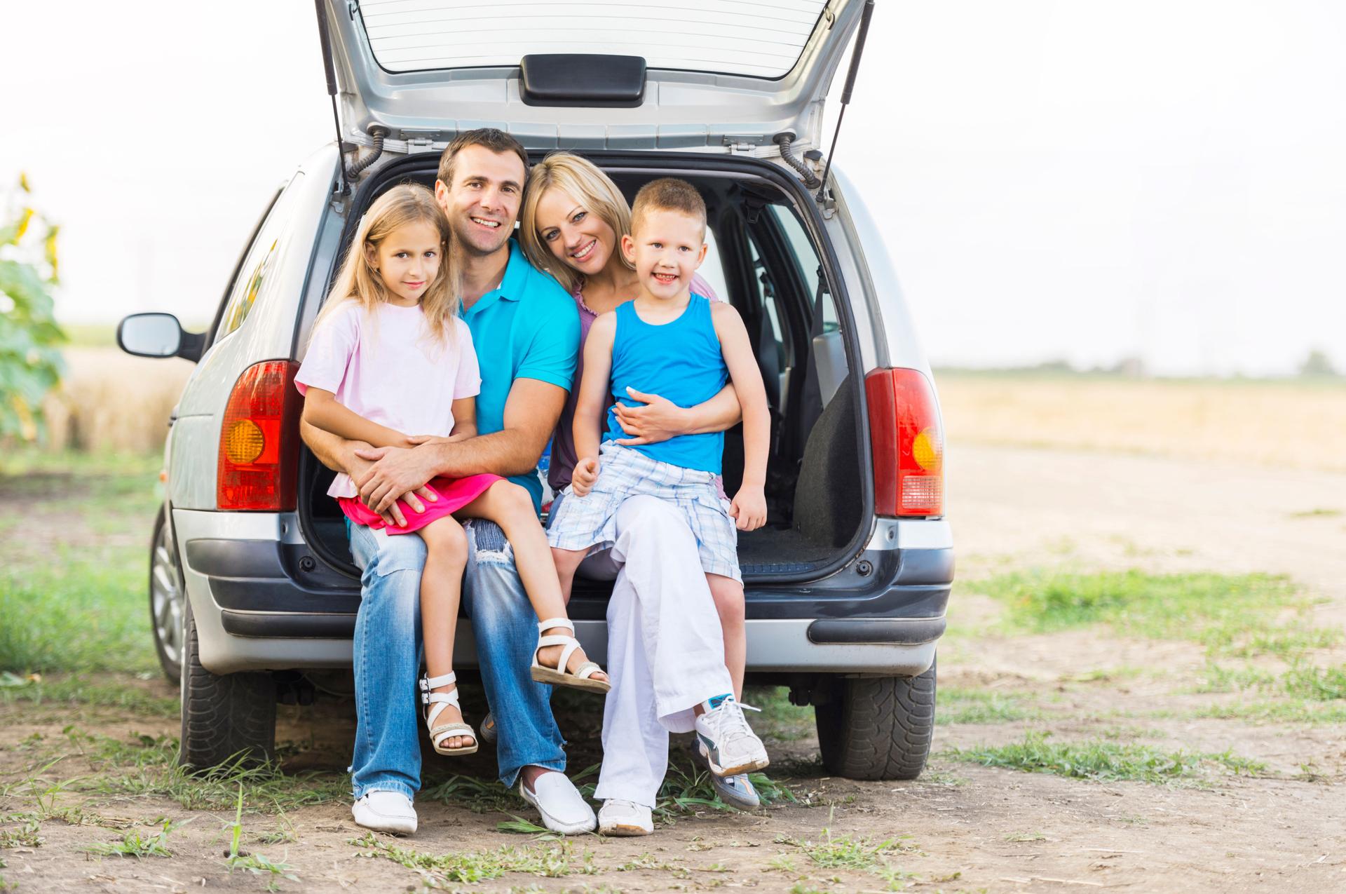Happy family sitting in a car trunk outdoors.