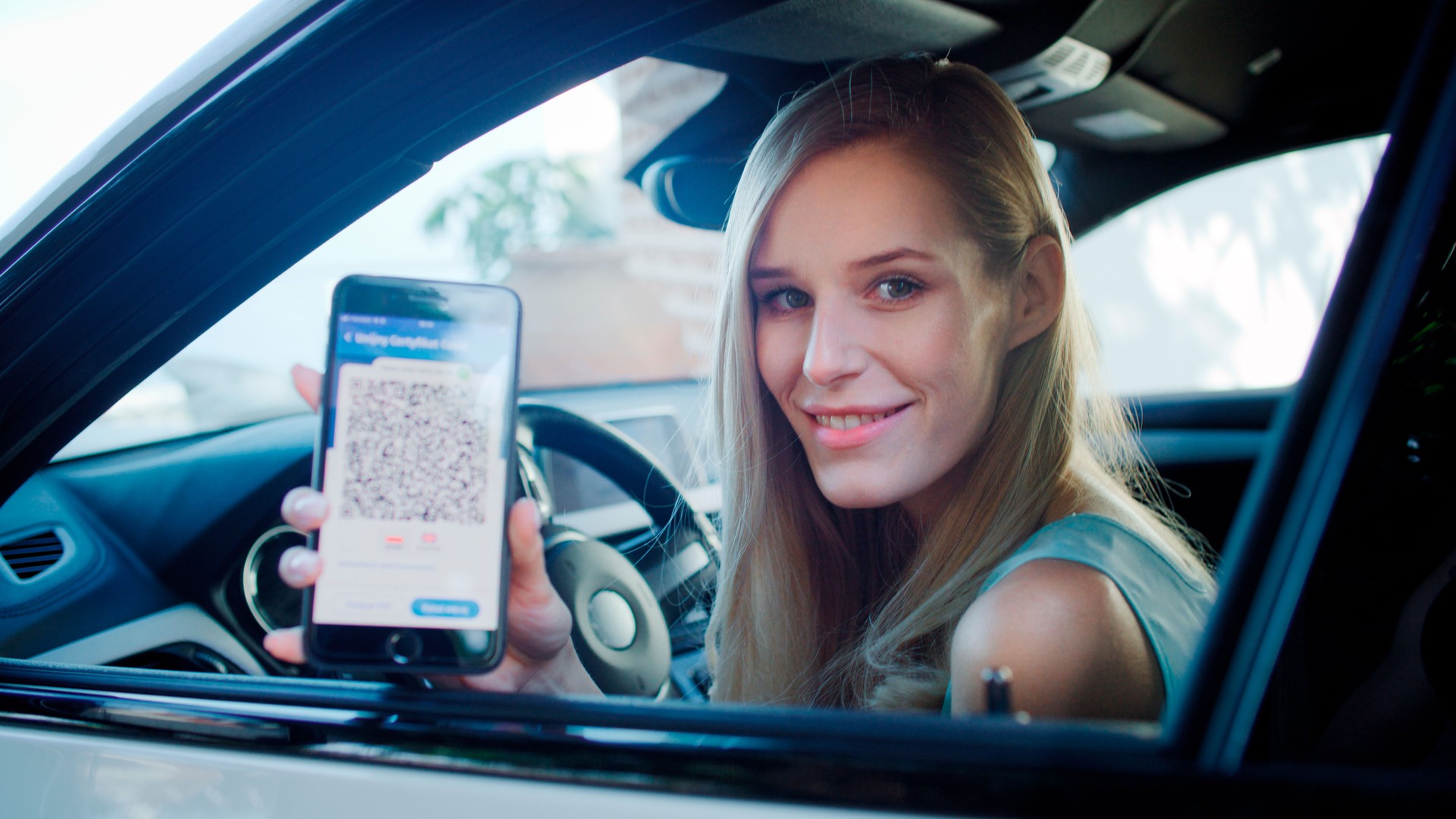 Female driver using digital vaccine passport app in mobile phone. Leaning out of the car window