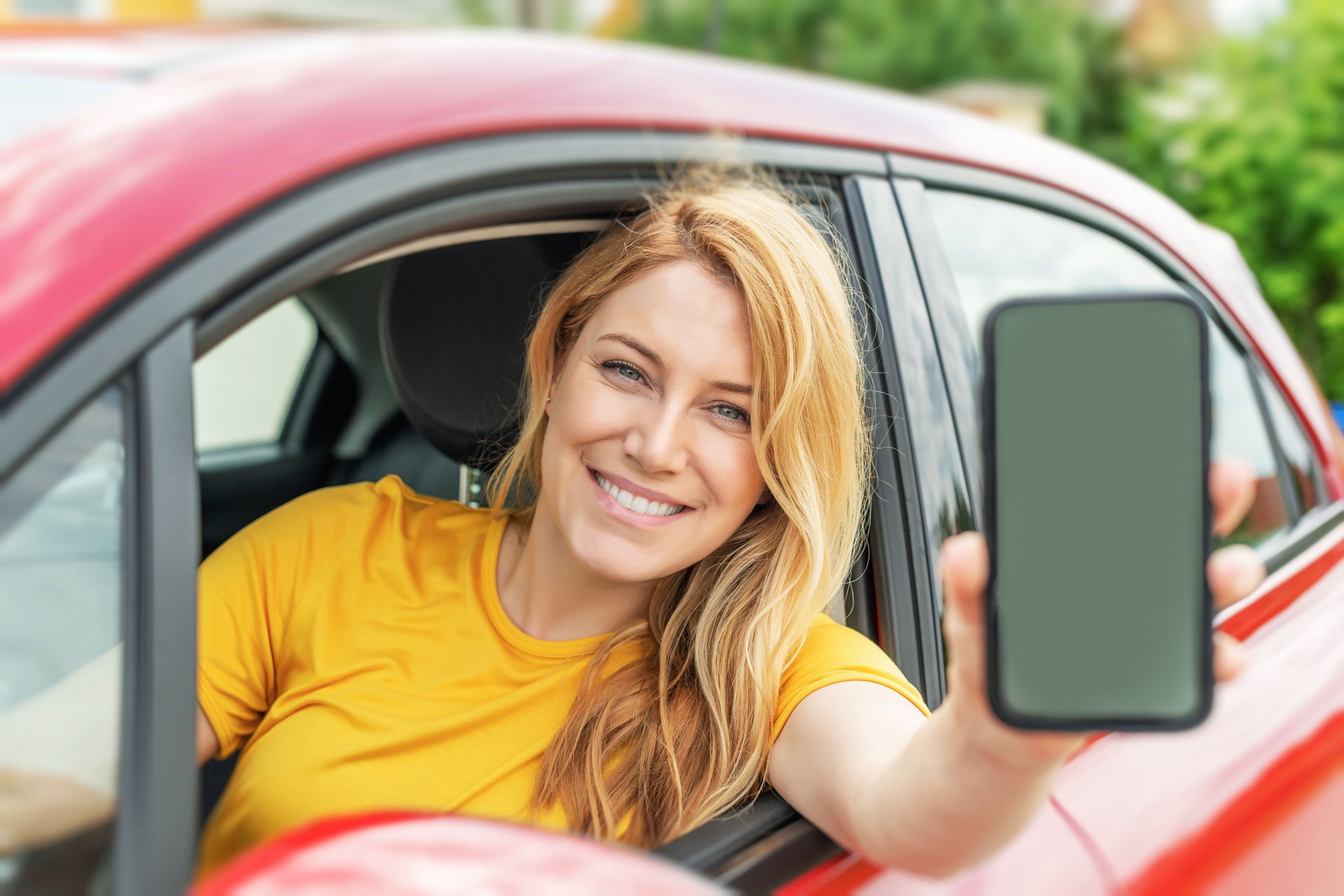 Young woman driving a car shows a smartphone screen.