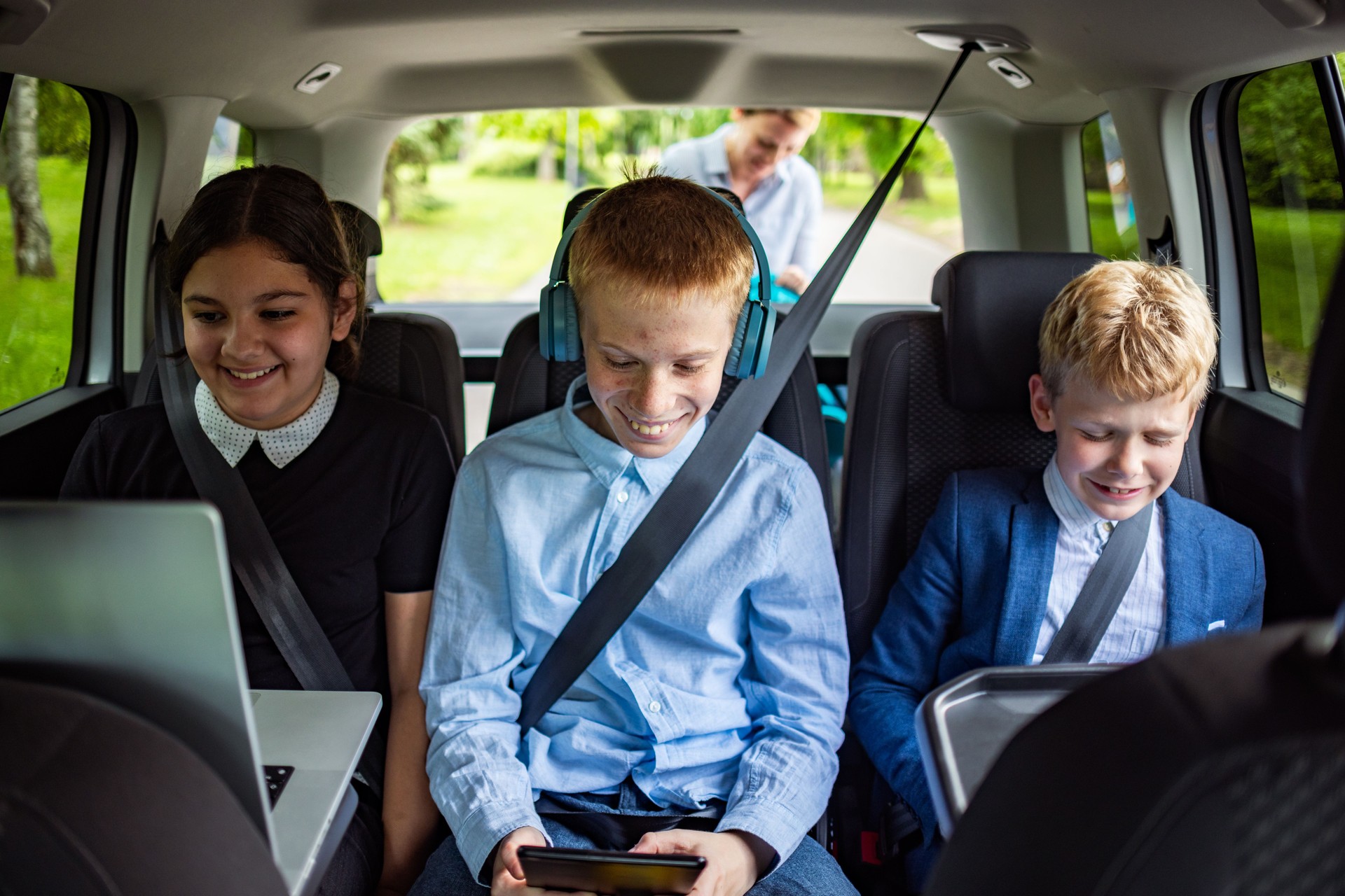Caucasian schoolboys and schoolgirl, doing homework while using a digital tablet and laptop connected to a car WiFi, while sitting in a backseat
