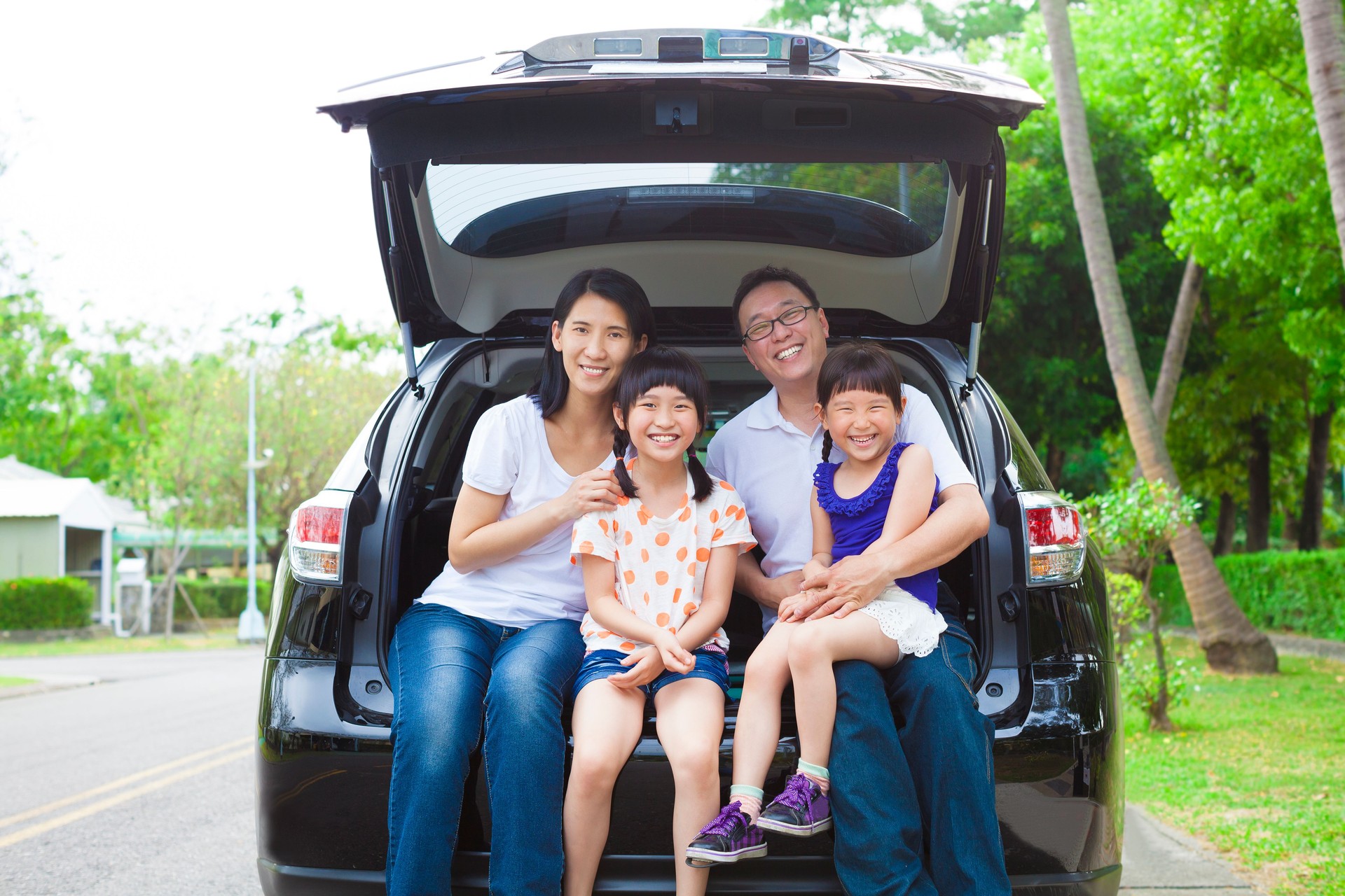 happy family sitting in the car and their house behind